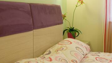 A bed with a patterned bedspread, a headboard, a wall-mounted light, and a potted plant.