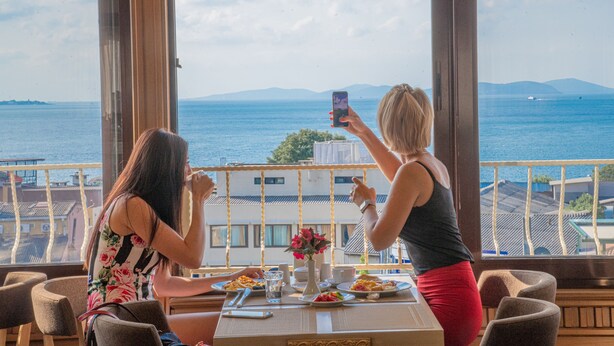 A dining area with a table set for two, overlooking a scenic view of the sea and distant mountains. - Kaftan Hotel (Istanbul)