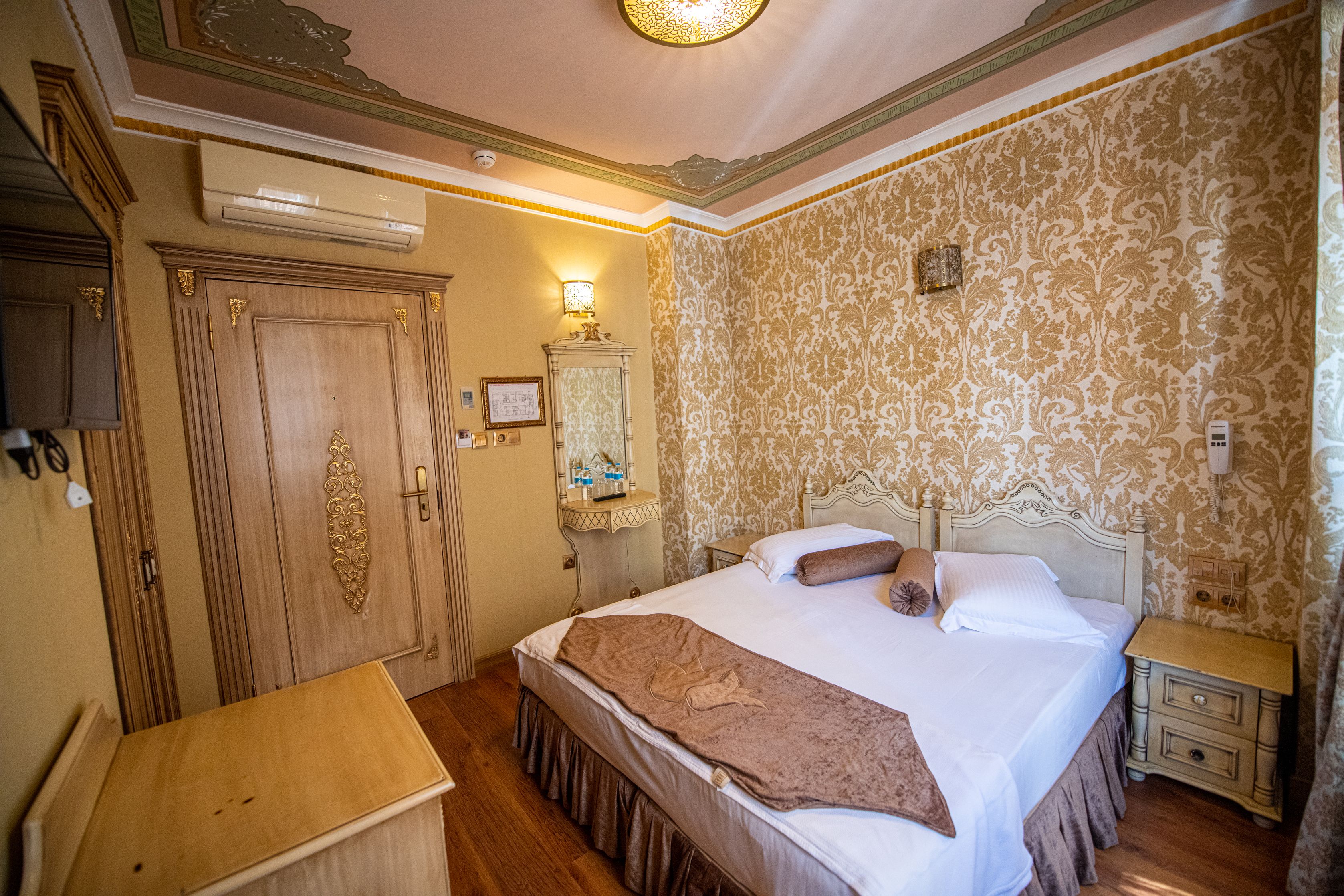 A hotel room with a large bed, wooden wardrobe, and a small bedside table.