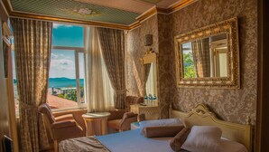 A hotel room with a large bed, a sitting area with a chair and a small table, a mirror on the wall, and a view of the sea through the window. - Kaftan Hotel (Istanbul)