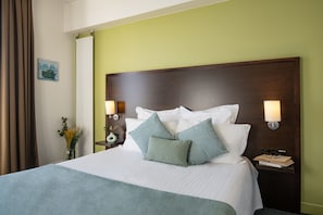 Una cama bien tendida con cabecera de madera, dos lámparas de noche y una mesita de noche con un florero.