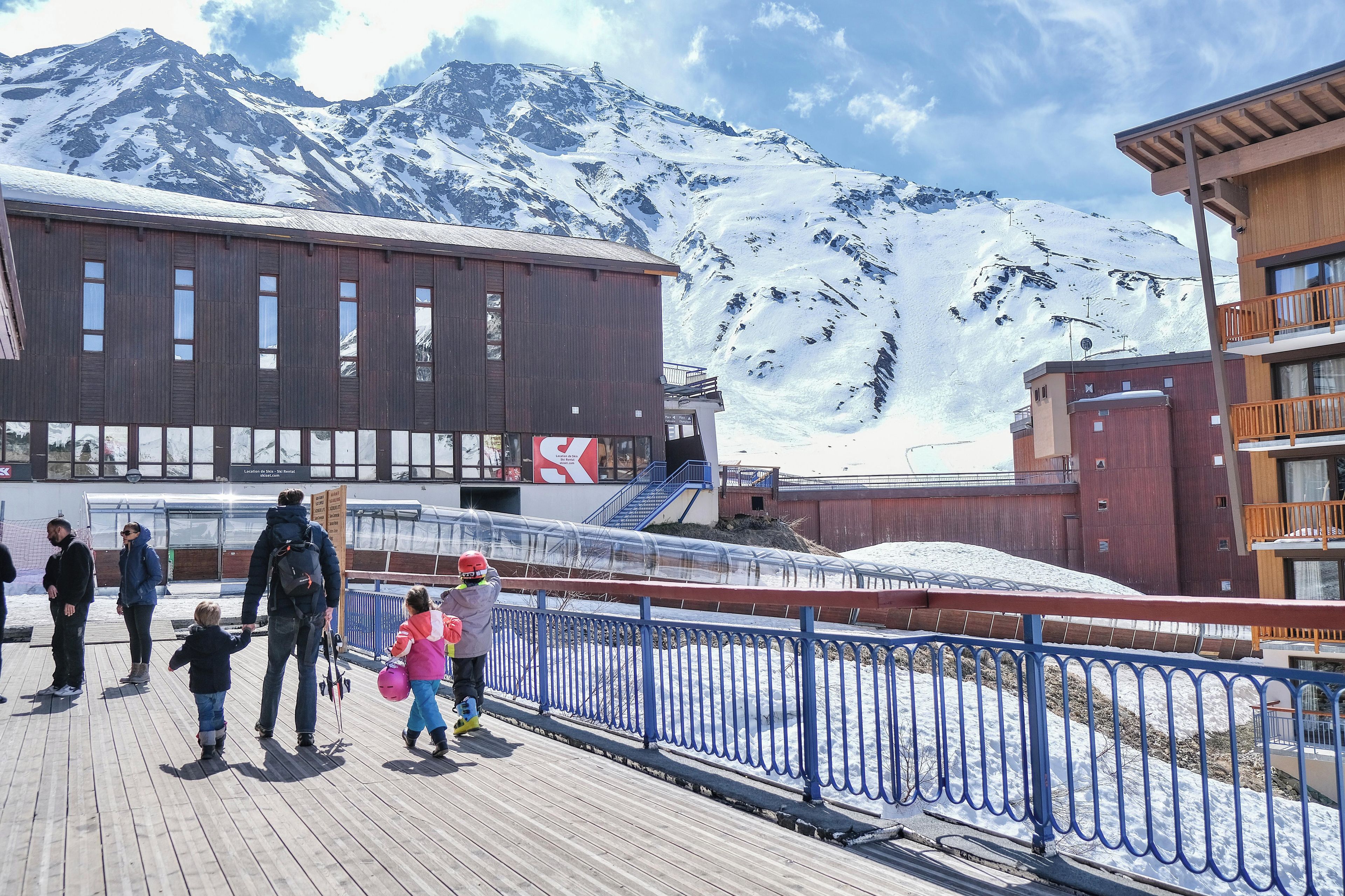 Une promenade en bois dotée d’une rambarde métallique, qui mène à un bâtiment où l’on peut louer du matériel de ski.