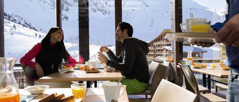 A breakfast setting with a mountain view, wooden tables, and a variety of breakfast items.