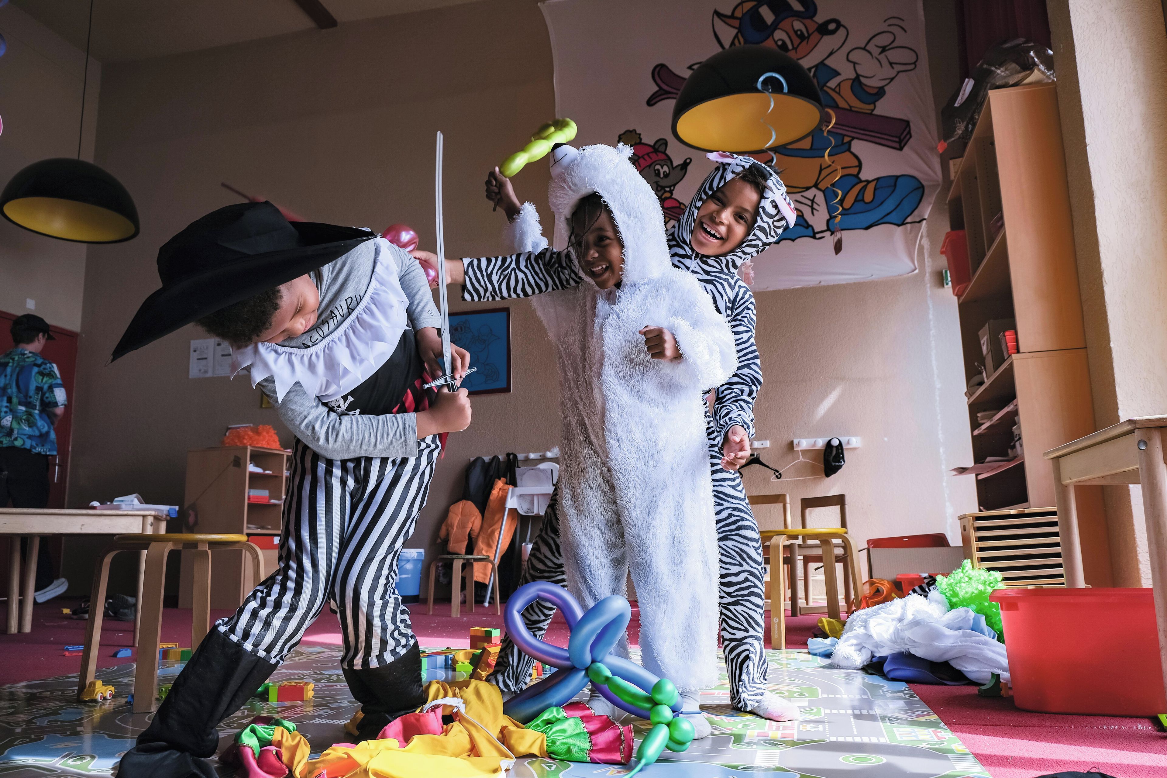 A room with a play area, a table, chairs, and a wall with cartoon characters.