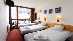 Une chambre d’hôtel avec trois lits, une télévision, un balcon avec vue sur les pistes de ski et des œuvres d’art accrochées au mur.