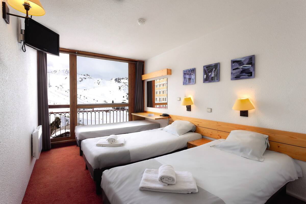 A hotel room with three beds, a TV, a balcony with a ski view, and artwork on the wall.