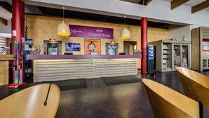 Un espace d’accueil avec un bureau en bois, deux lampes suspendues, une horloge et un panneau indiquant « Belambra Hôtel L’Aiguille Rouge ».