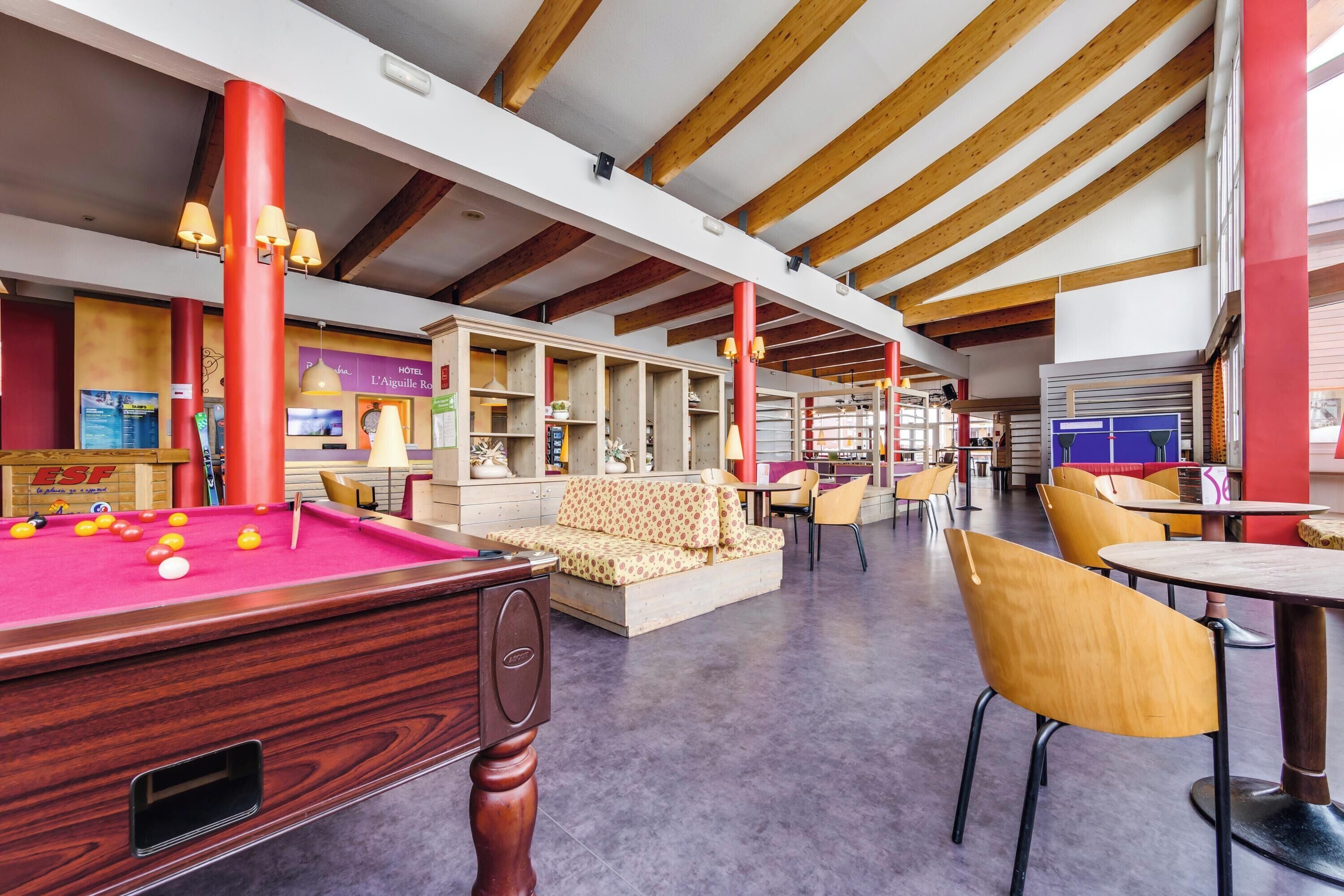 A billiards room with a pool table, seating area, and wooden beams on the ceiling.