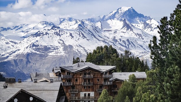 Un chalet de montagne doté de plusieurs balcons et offrant une vue sur des sommets enneigés.