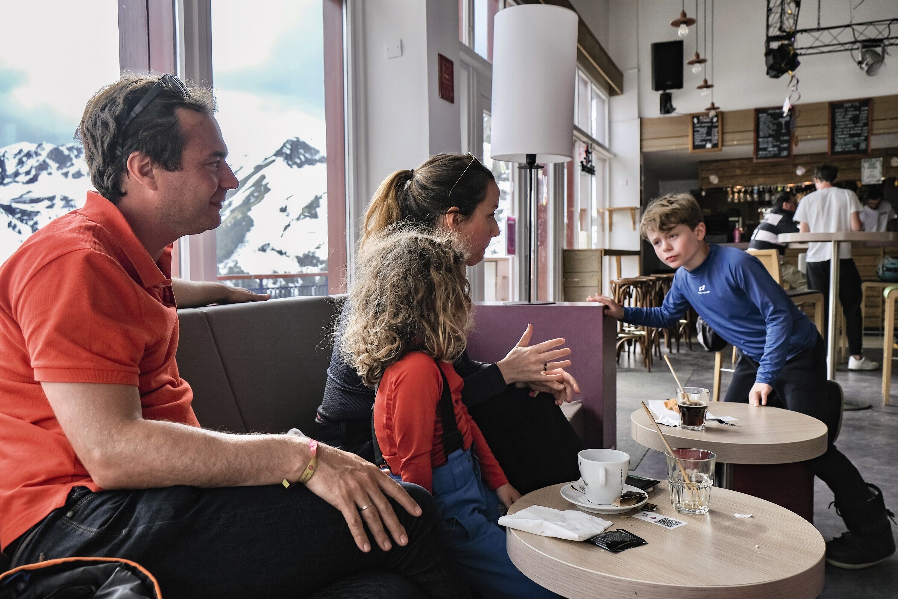 Un café chaleureux offrant une vue sur des montagnes enneigées, avec des tables rondes, des sièges confortables et une ambiance décontractée.
