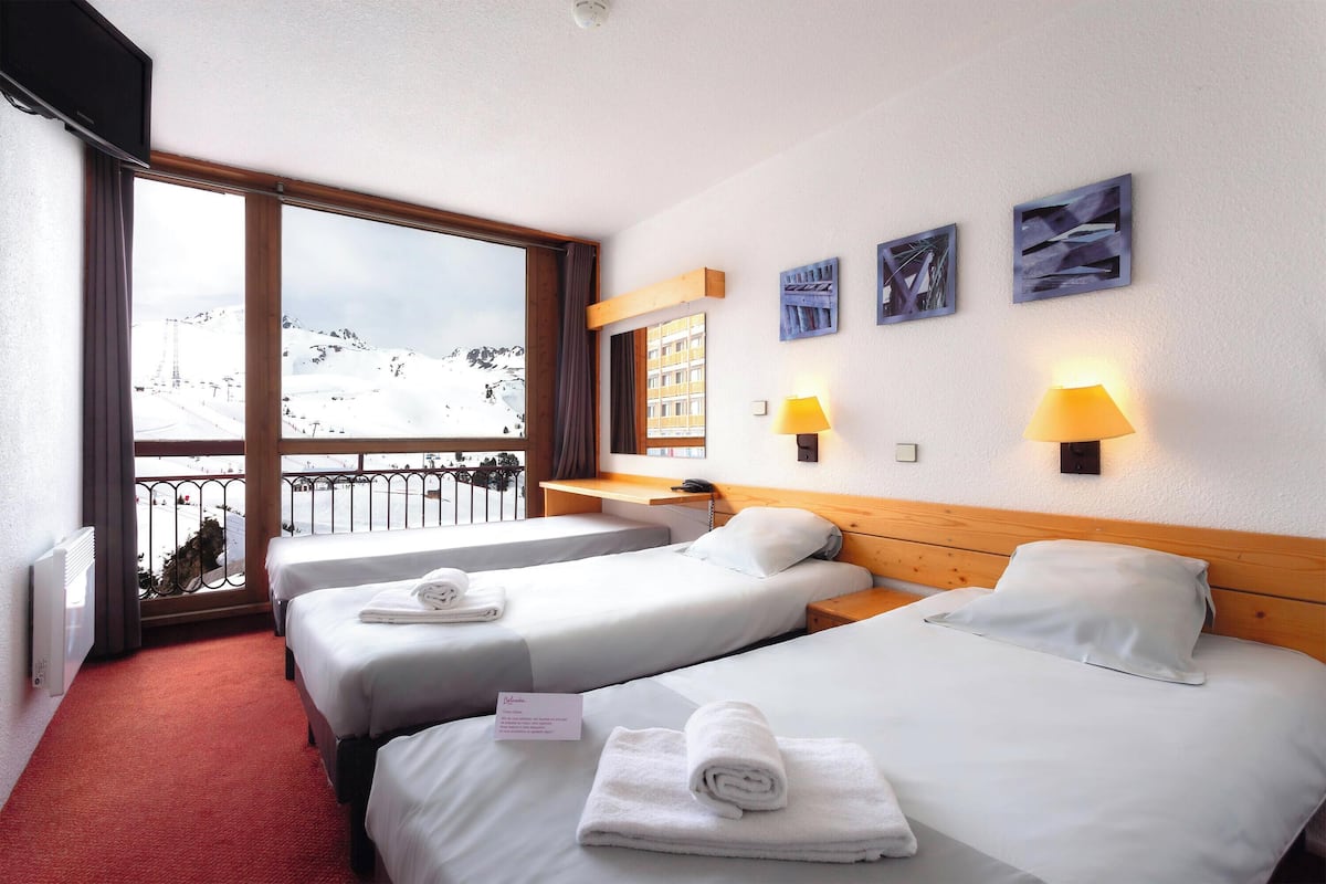 A hotel room with two beds, a balcony with a mountain view, and artwork on the wall.