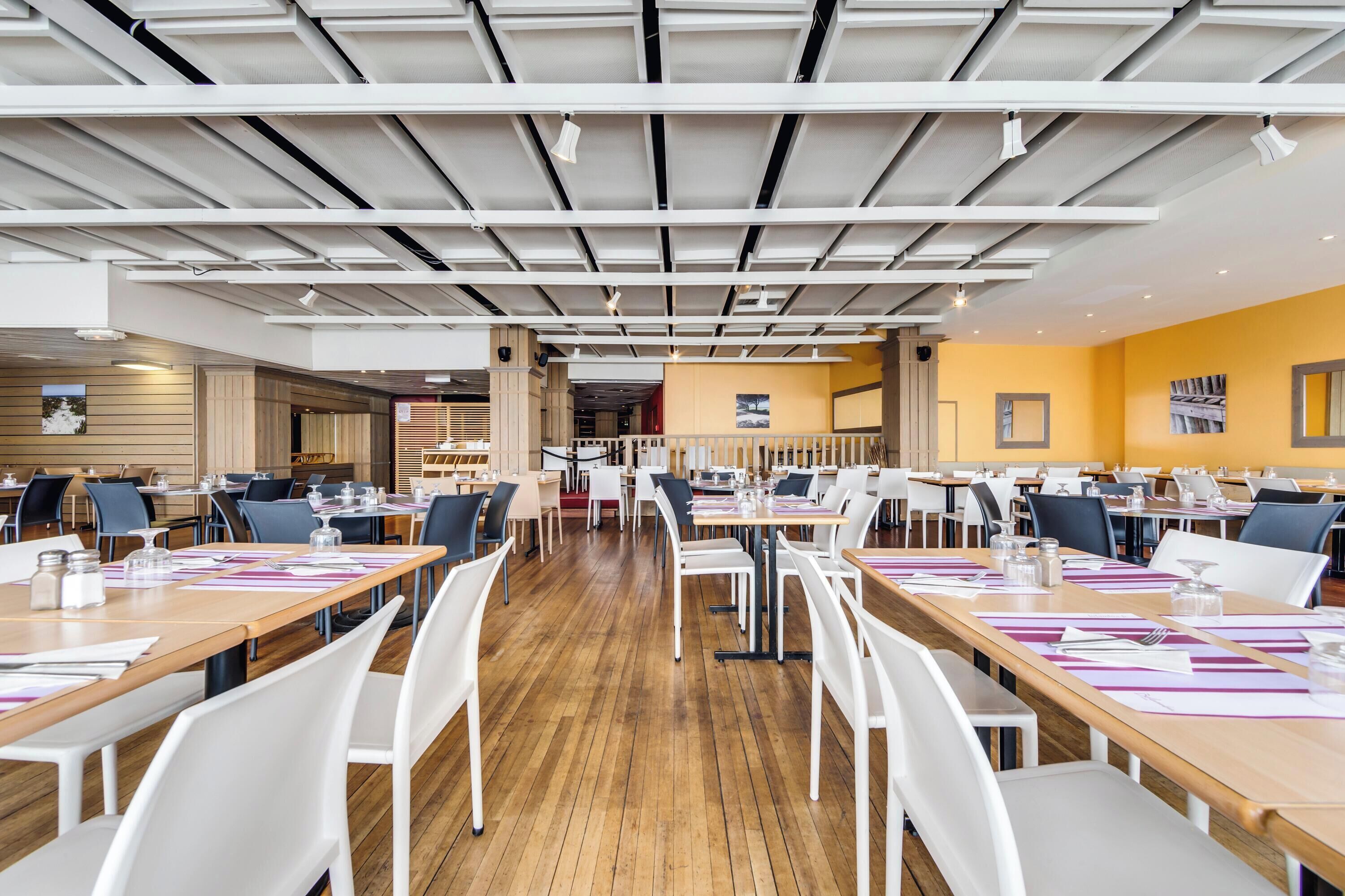 Un vaste espace dédié à la salle à manger, avec de nombreuses tables et chaises, un plancher en bois et un design moderne au niveau du plafond.