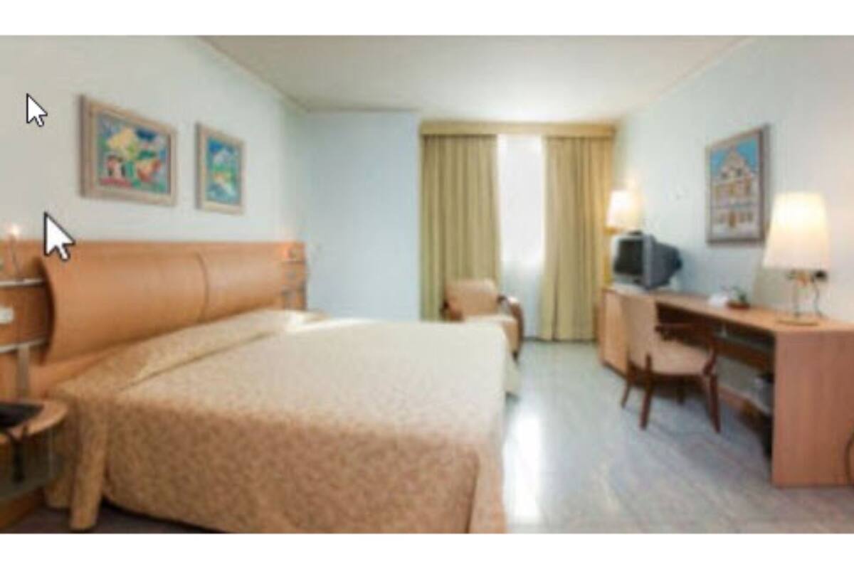 Ein Hotelzimmer mit einem großen Bett, einem Schreibtisch, einem Sessel, einem Fernseher und zwei Bildern an der Wand.