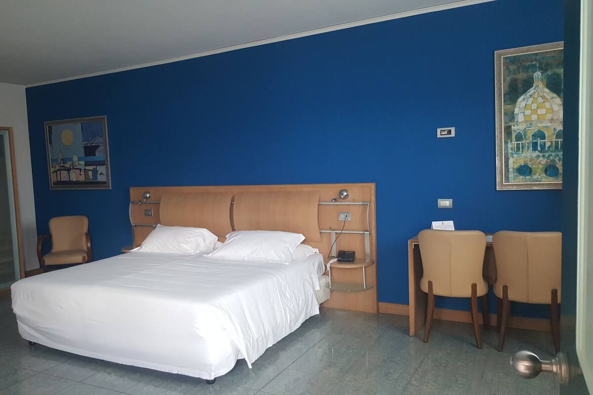 Ein Hotelzimmer mit einem großen Bett, einem Schreibtisch, zwei Stühlen, einem Kleiderschrank und einem Bild an der Wand.