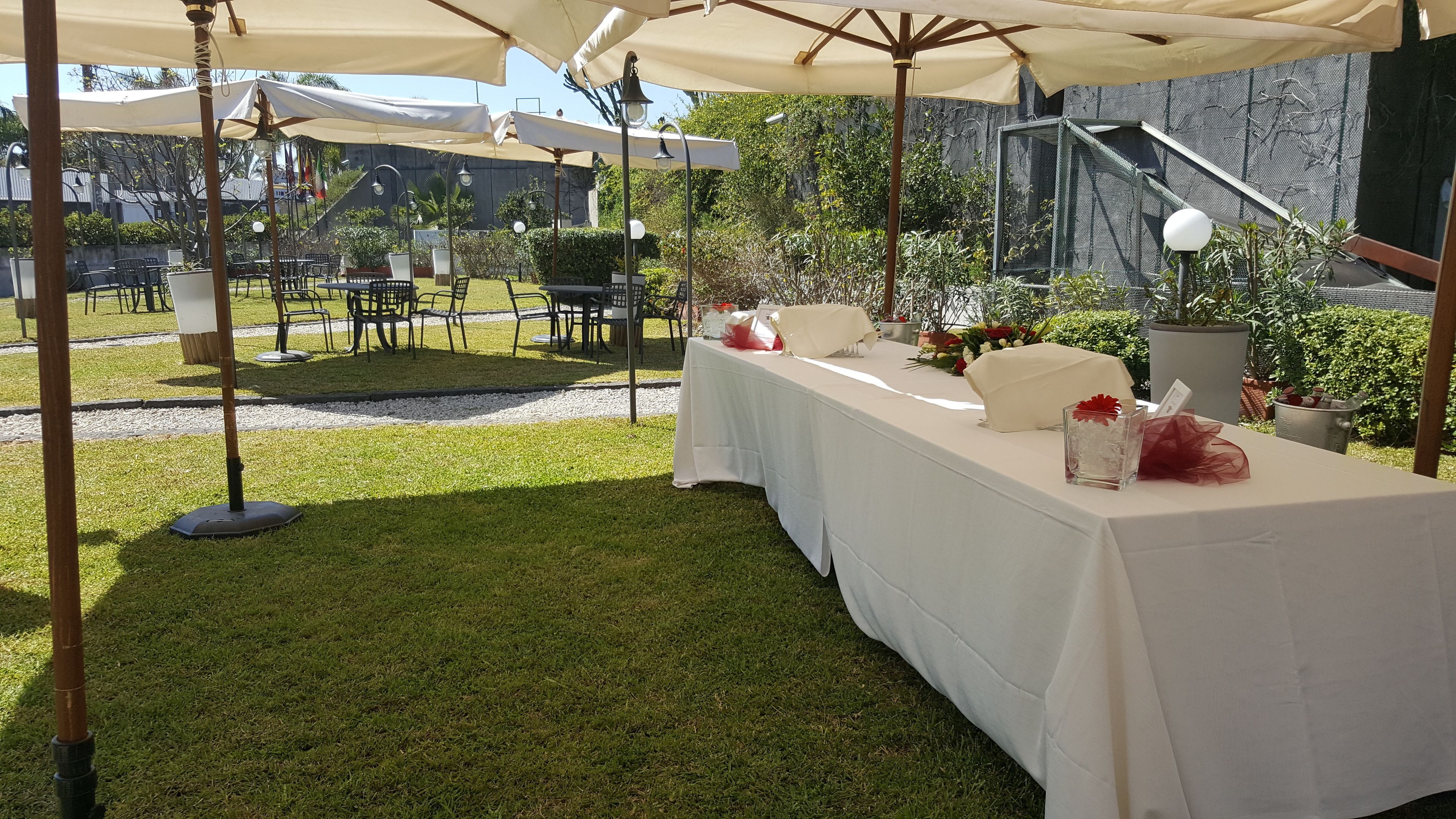 Area pranzo all'aperto con tavoli coperti da tovaglie bianche, ombrelloni e sedie.