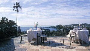 Une terrasse extérieure avec deux tables dressées pour le dîner, offrant une vue sur un paysage côtier.
