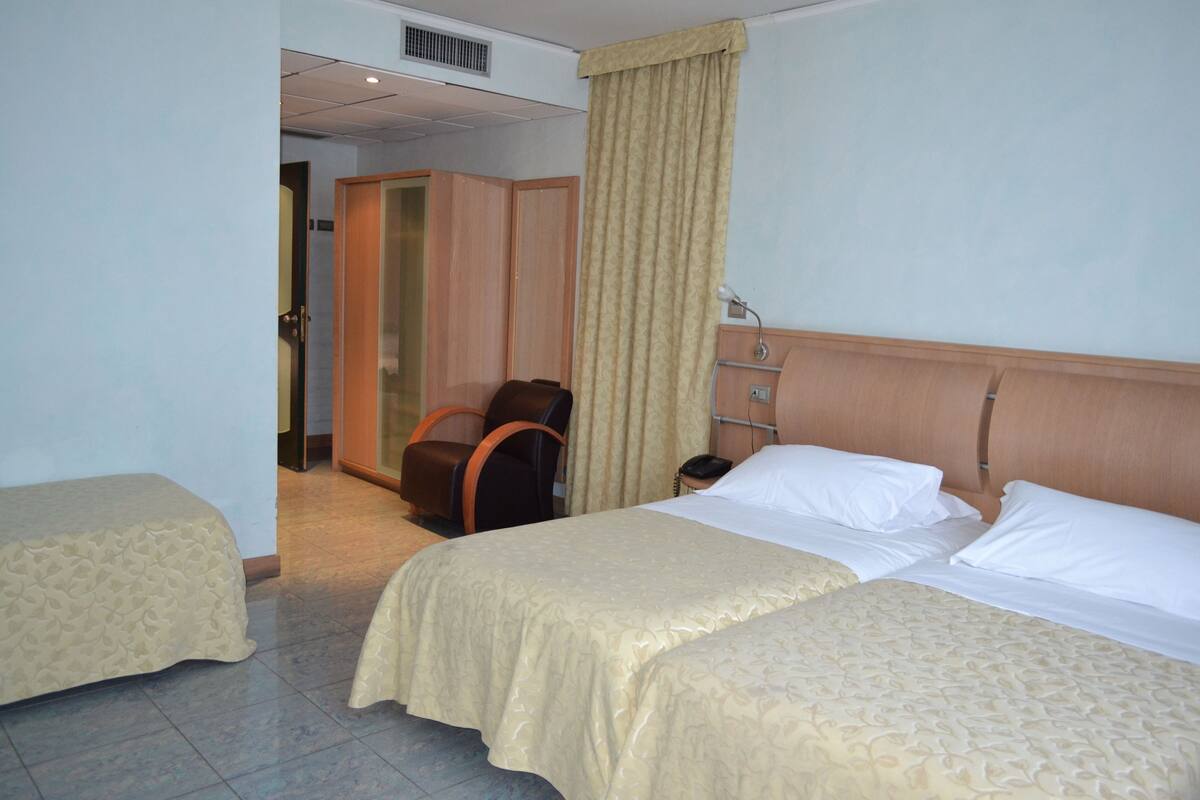 Ein Hotelzimmer mit zwei Betten, einem Holzkopfteil, einem Schreibtisch, einem Stuhl und einem Vorhang.