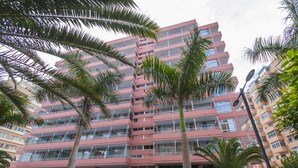 Een hotel met meerdere verdiepingen, balkons, palmbomen en een parkeerplaats.