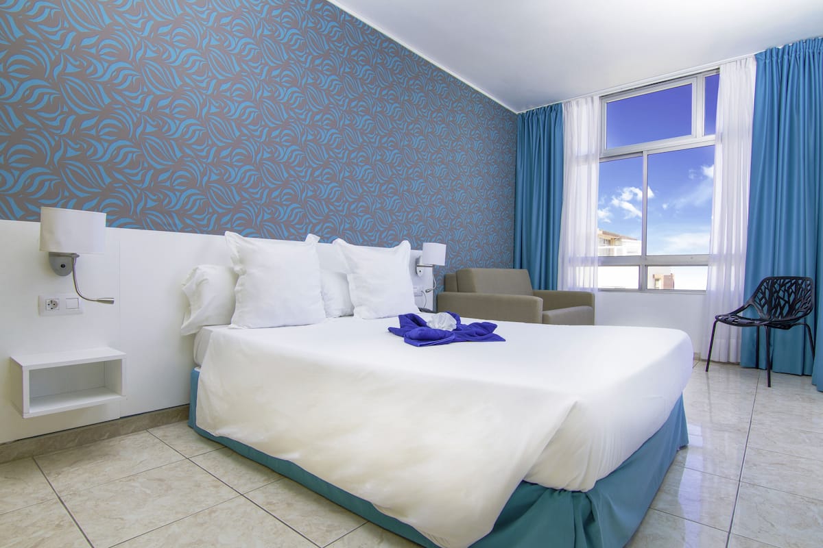 Habitación de hotel con una cama grande, una silla, un escritorio y una ventana con cortinas.