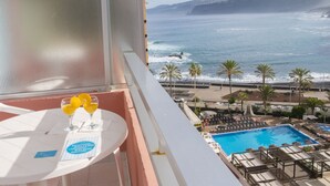 Een balkon met een zwembad, ligbedden en uitzicht op zee.