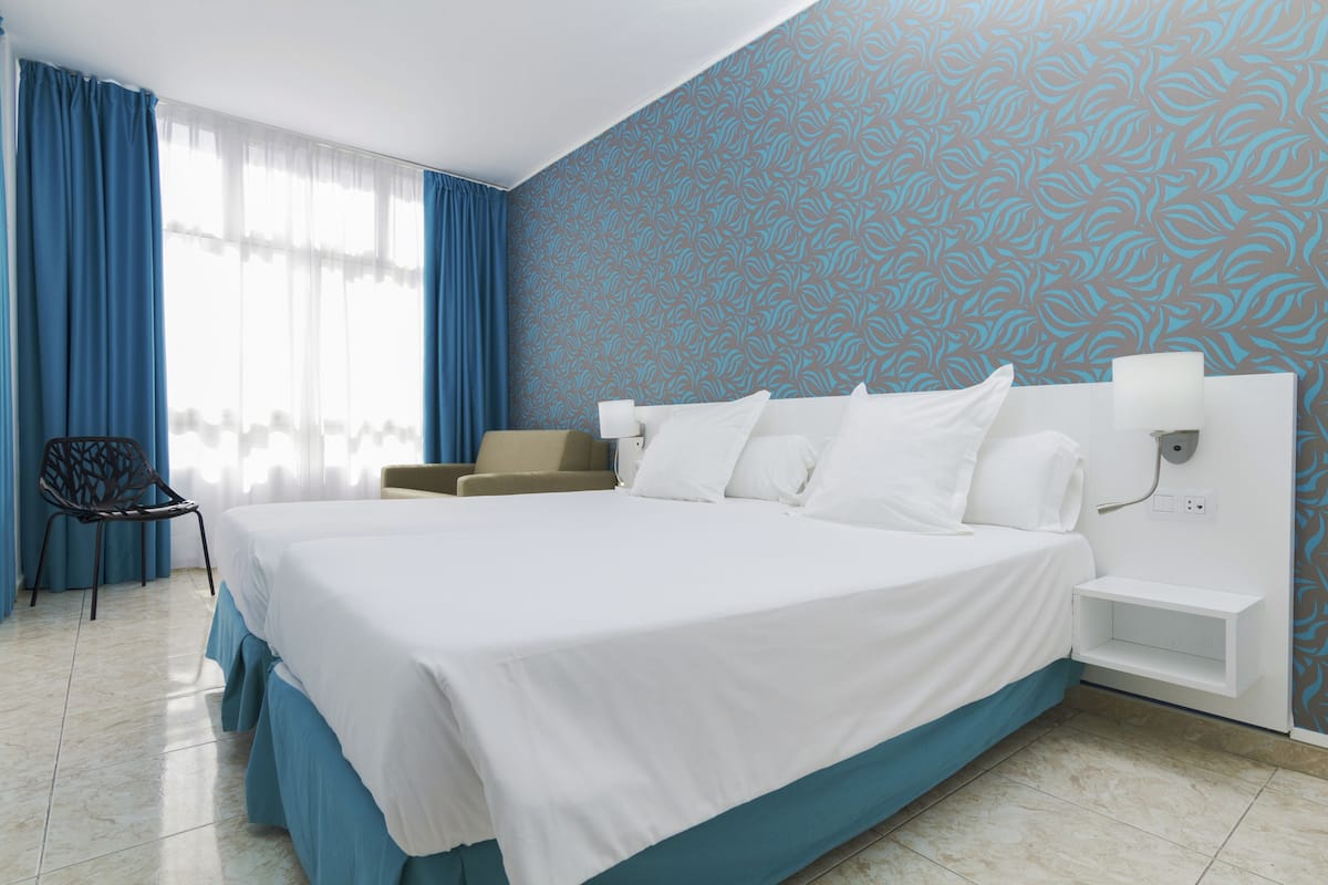 Habitación de hotel con una cama grande, una silla, una mesita de noche y un papel tapiz estampado.