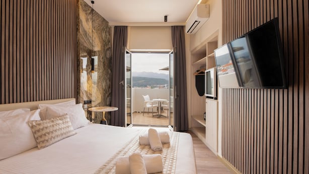 Une chambre d’hôtel avec un lit, une télévision, un balcon avec une chaise et une vue sur les montagnes.