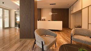 Un espace d’accueil moderne comprenant un comptoir de réception en bois, deux fauteuils rembourrés et une table noire agrémentée d’une plante.