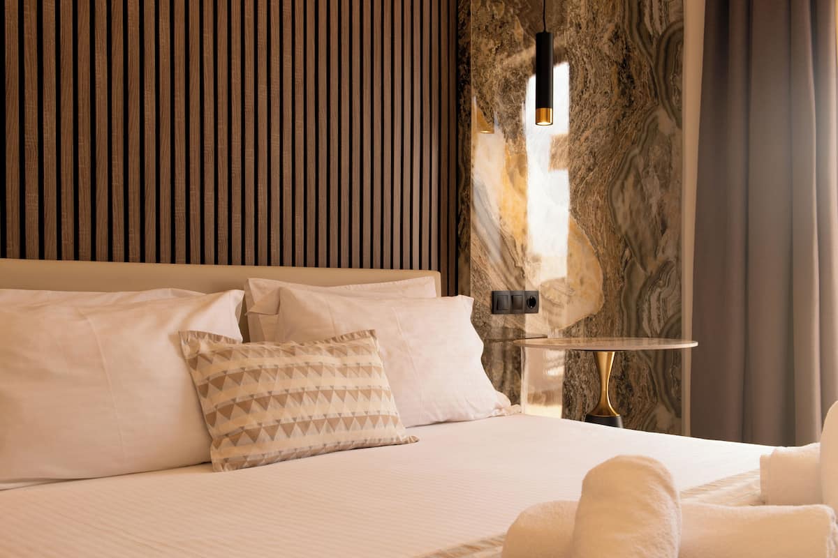 A hotel room with a bed, pillows, a nightstand, and a lamp.