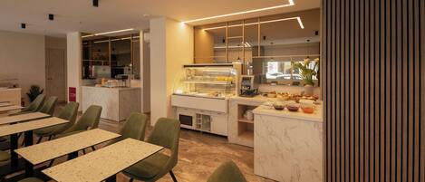 A modern dining area with green chairs, a marble counter, and a kitchen in the background.
