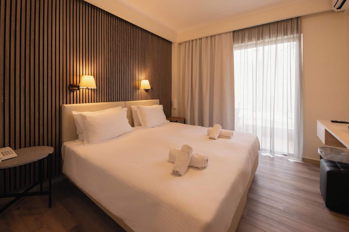 A hotel room with a large bed, two bedside lamps, a desk with a phone, and a window with curtains.