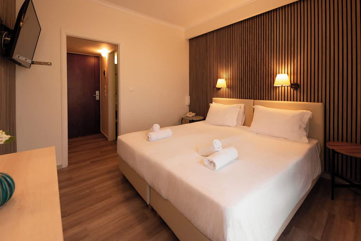 A hotel room with a bed, bedside tables, a TV mounted on the wall, and a wooden panel wall.