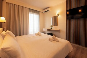 Habitación de hotel con una cama grande, una mesita de noche, un espejo y un televisor montado en la pared.