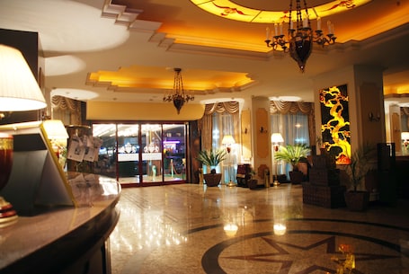 A hotel lobby with a chandelier, potted plants, and a reception desk.