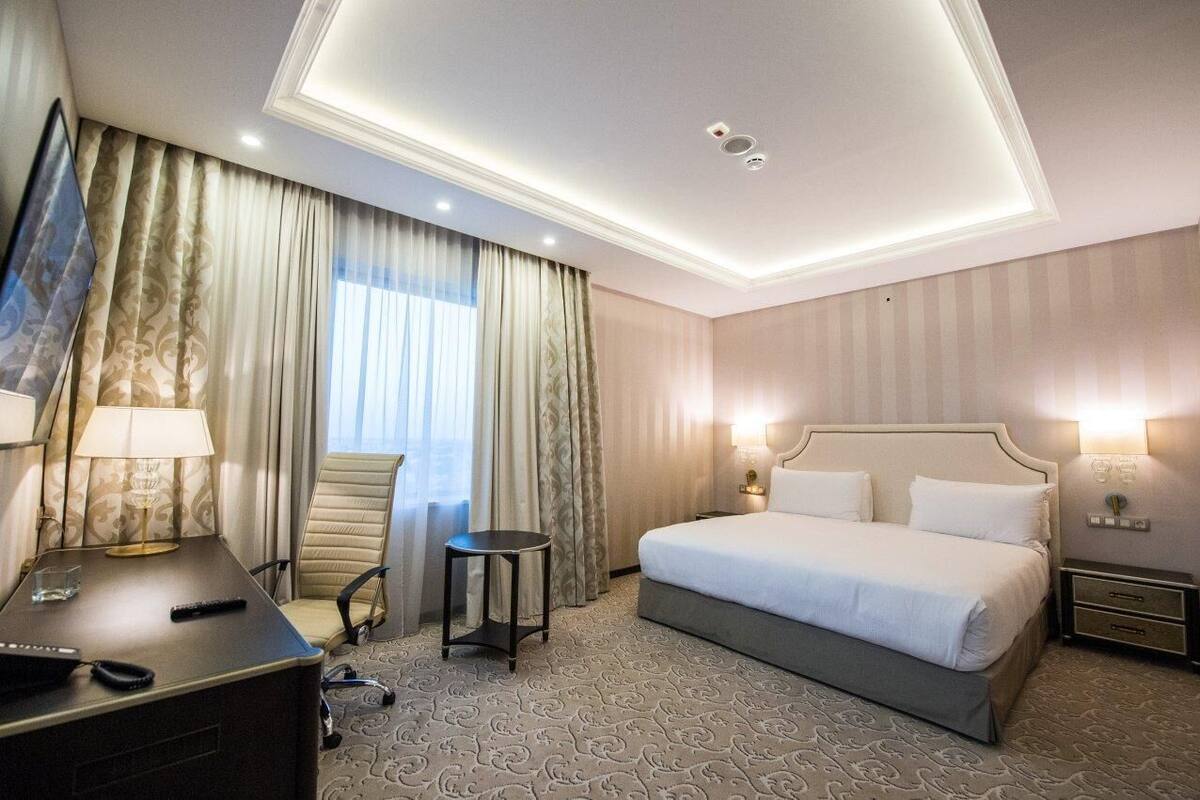 Een hotelkamer met een groot bed, een bureau met lamp, een stoel en een televisie.