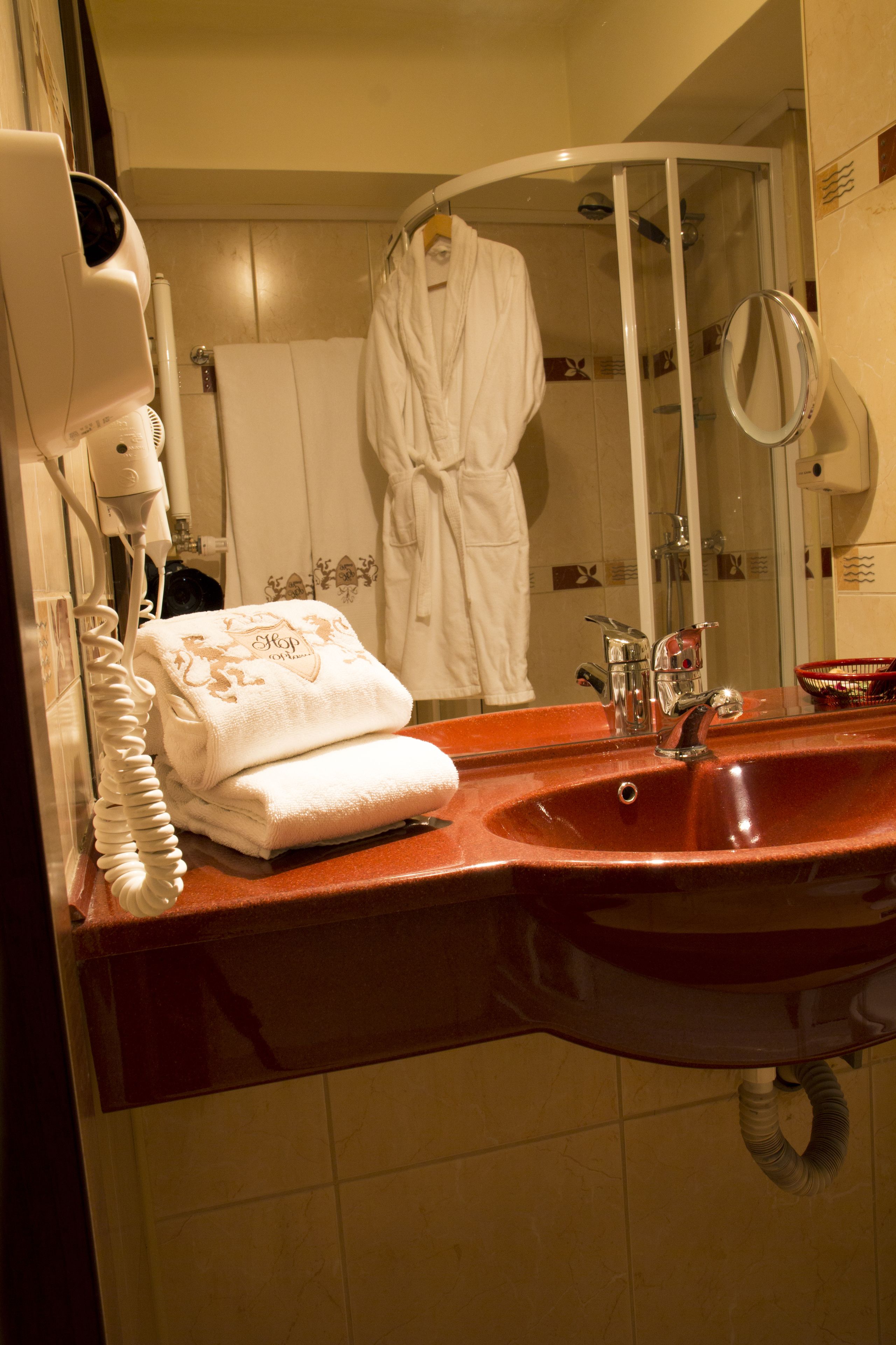 Een badkamer met een rode wastafel, een handdoek, een haardroger en een douche met glazen wanden.