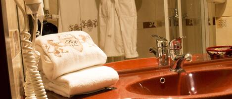 A bathroom with a red sink, a towel, a hairdryer, and a glass-enclosed shower.
