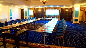 Une salle de conférence avec une longue table, une moquette bleue et des lustres.