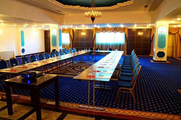 Un salón de conferencias con una larga mesa, alfombra azul y candelabros.