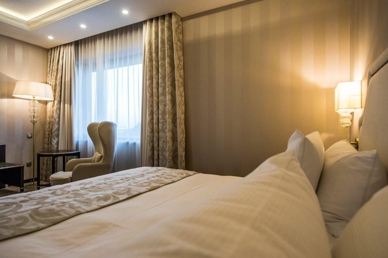 A hotel room with a large bed, a chair, a desk, and a lamp.