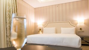 Une chambre d’hôtel avec un grand lit, deux lampes de chevet, une table de nuit et un verre de vin posé sur une table.