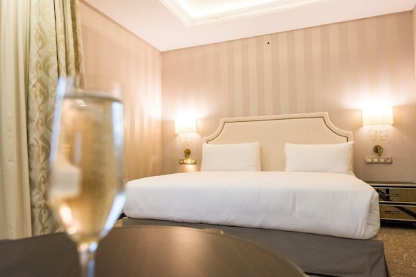 Ein Hotelzimmer mit einem großen Bett, zwei Nachttischlampen, einem Nachttisch und einem Glas Wein auf einem Tisch.