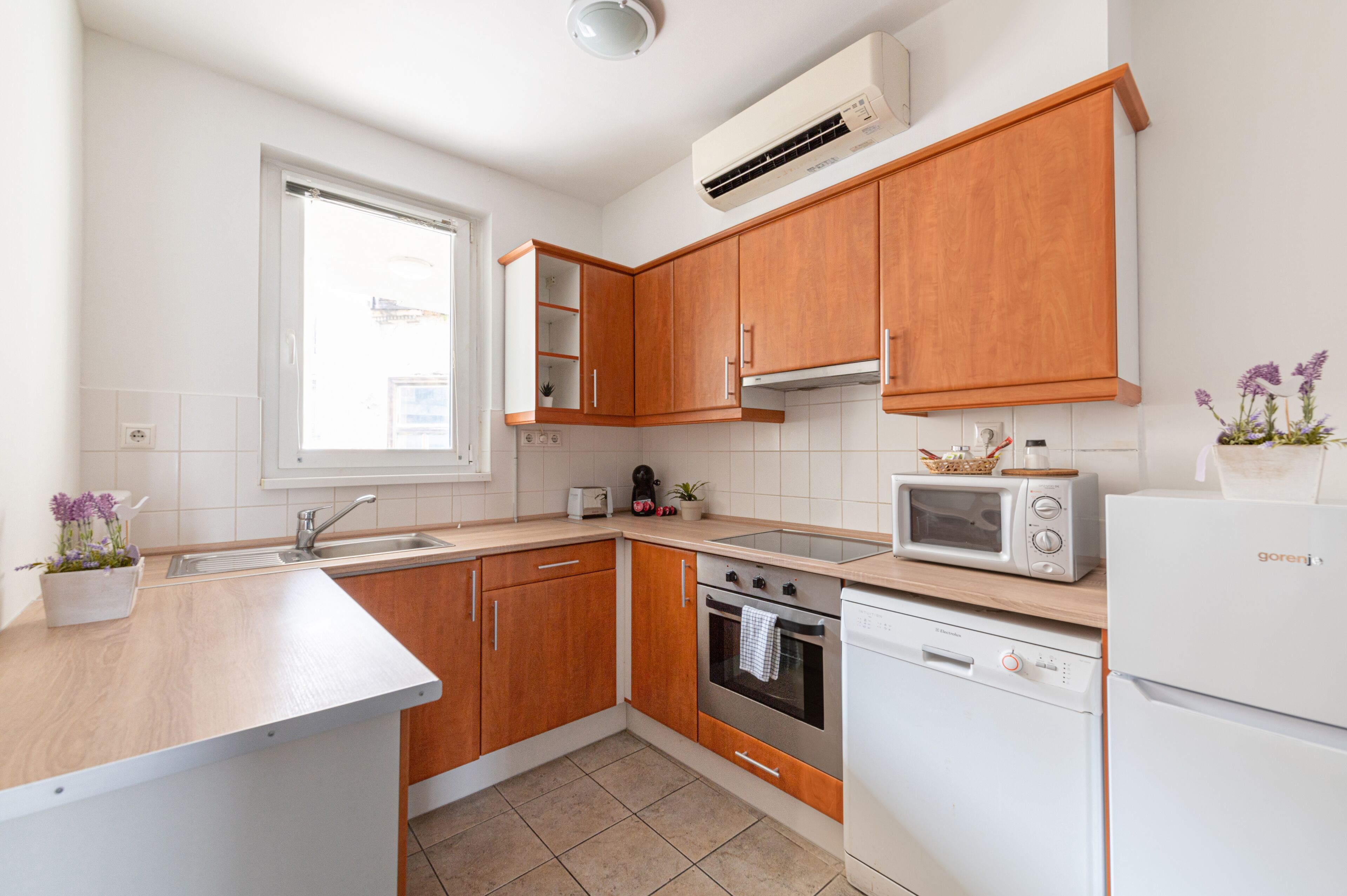 Una cucina moderna con mobili in legno, forno a microonde integrato, lavastoviglie e una finestra che lascia entrare luce naturale.