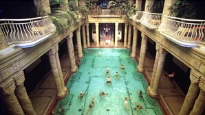 A swimming pool with multiple columns and railings, surrounded by a covered area with a balcony. - Nova Apartments (Budapest)