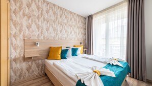 A hotel room with a large bed, a wooden headboard, and a window with curtains. - Nova Apartments (Budapest)