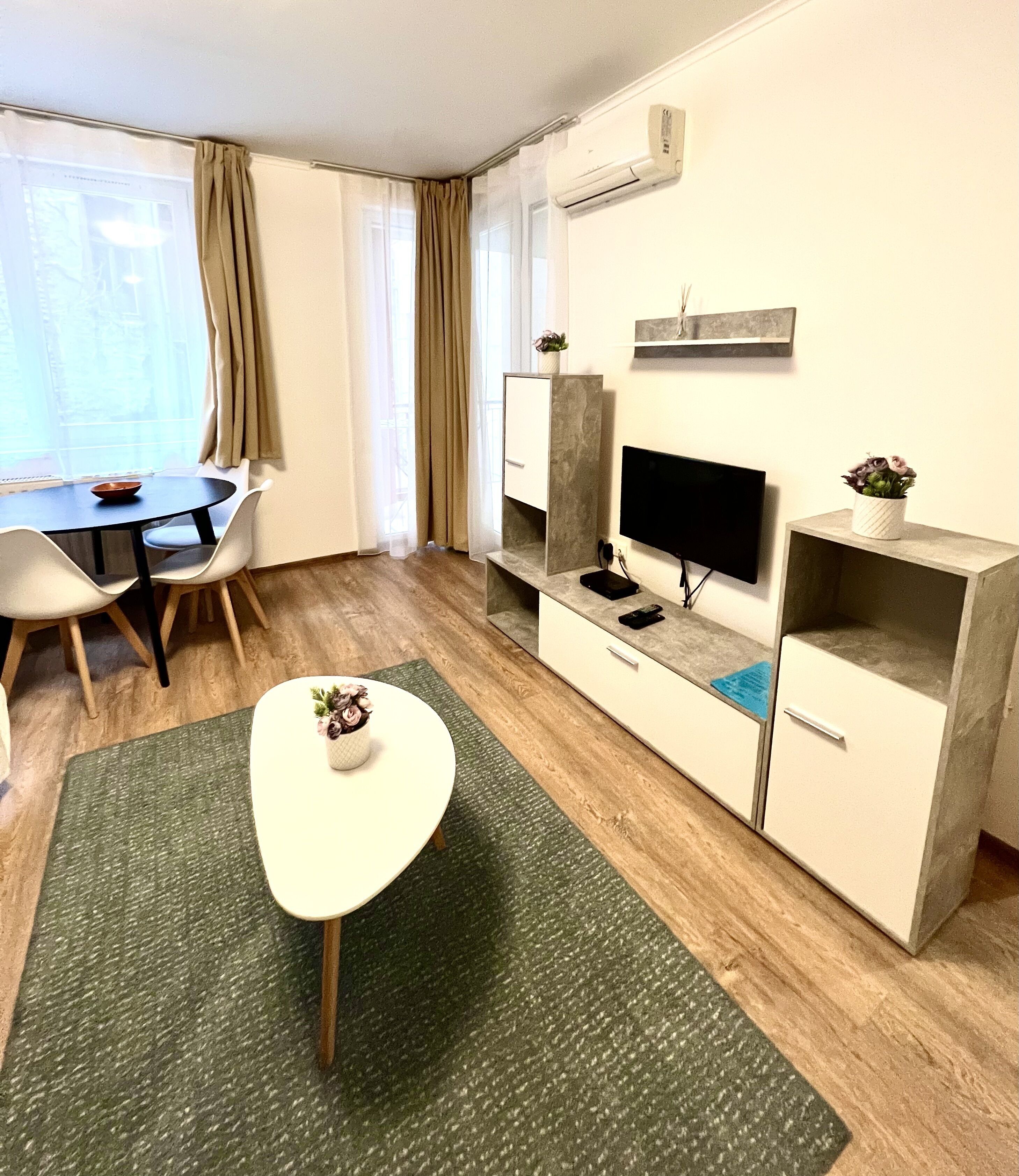 Een moderne hotelkamer met een eettafel, stoelen, een televisie, een kast en een kleine plant.