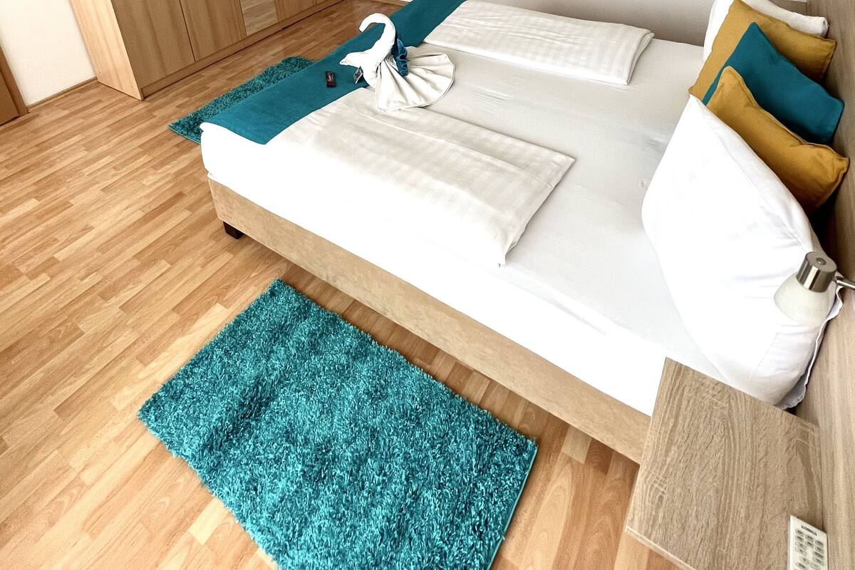 Quarto com cama, guarda-roupa, um objeto decorativo na parede e uma mesinha.