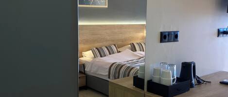 Camera d'albergo con un letto, comodini, uno specchio e una scrivania in legno con una macchina del caffè e tazze.