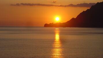 Un coucher de soleil sur une mer calme, avec la silhouette d’une montagne en arrière-plan.