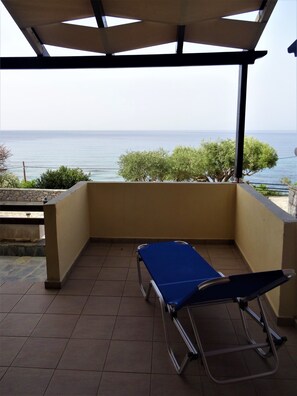 Un balcón con vista al mar, un tapete azul y una silla de metal.