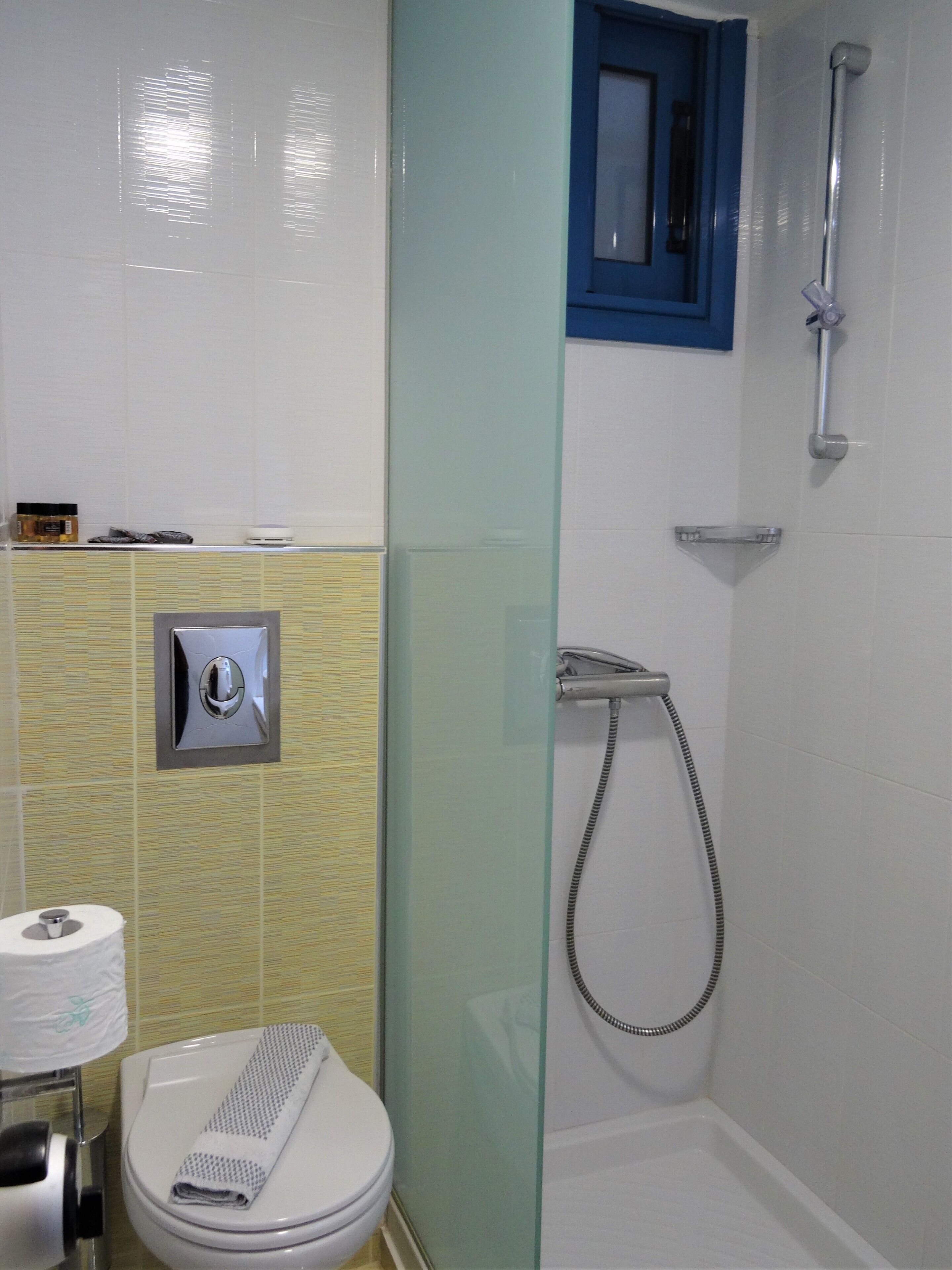 Un baño con inodoro, ducha con mampara de vidrio y una toalla sobre el asiento.